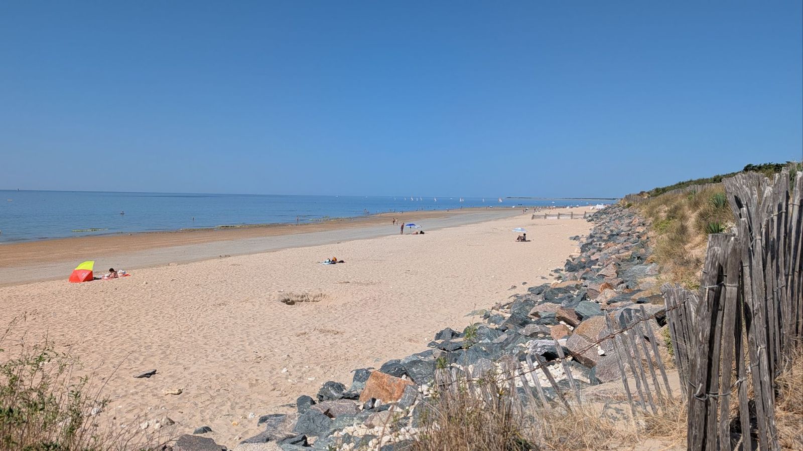 Breed zandstrand met een houten afrastering langs de duinrand